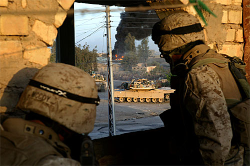 During the First Battle of Fallujah, U.S. Marines from the 1st Marine Regiment take cover as an M1A1 Abrams from the 1st Tank Battalion fires at a building where insurgent snipers are positioned.