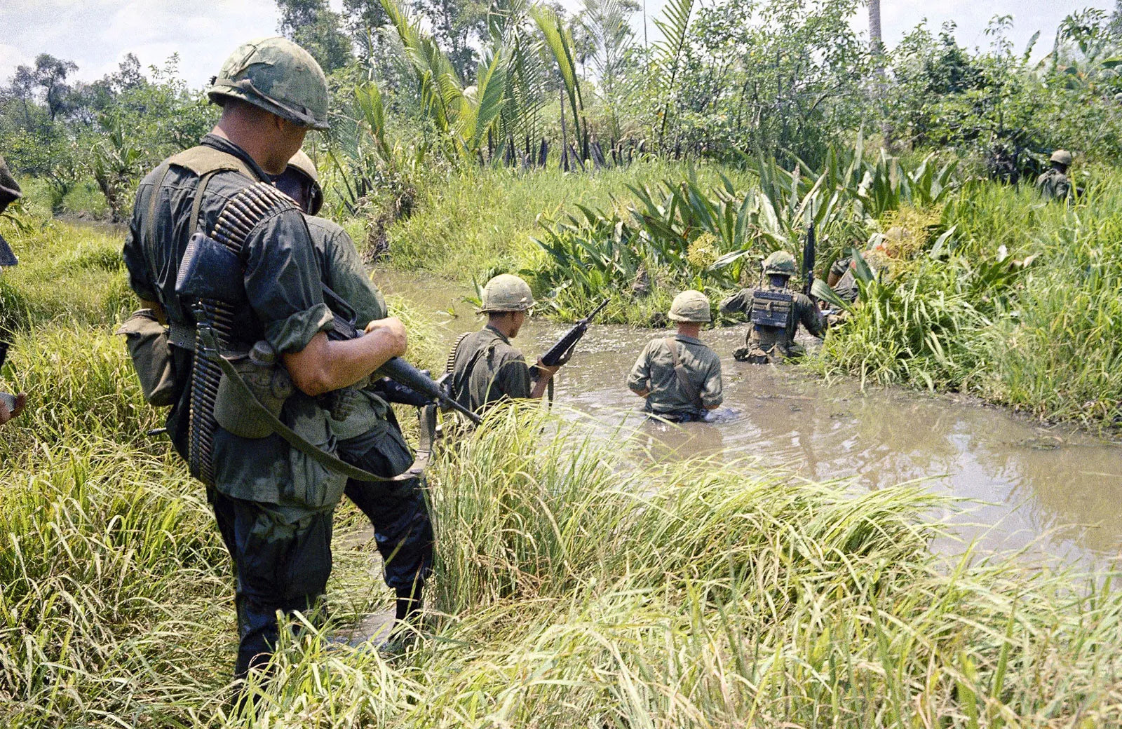 US Marines navigating through a marshy swamp during the Vietnam War in 1965, representing the Tactically Acquired USMC Vietnam War merchandise collection.